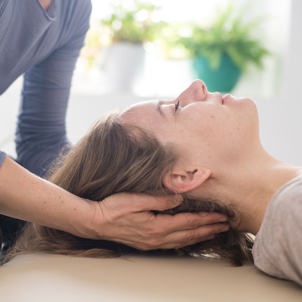 Somatic therapist gently supports client’s head during bodywork session
