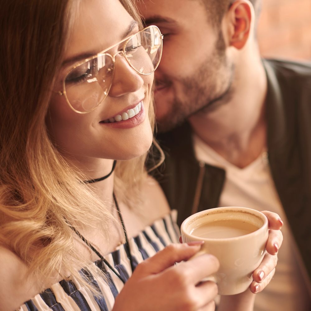 Man whispering to smiling woman holding coffee mug