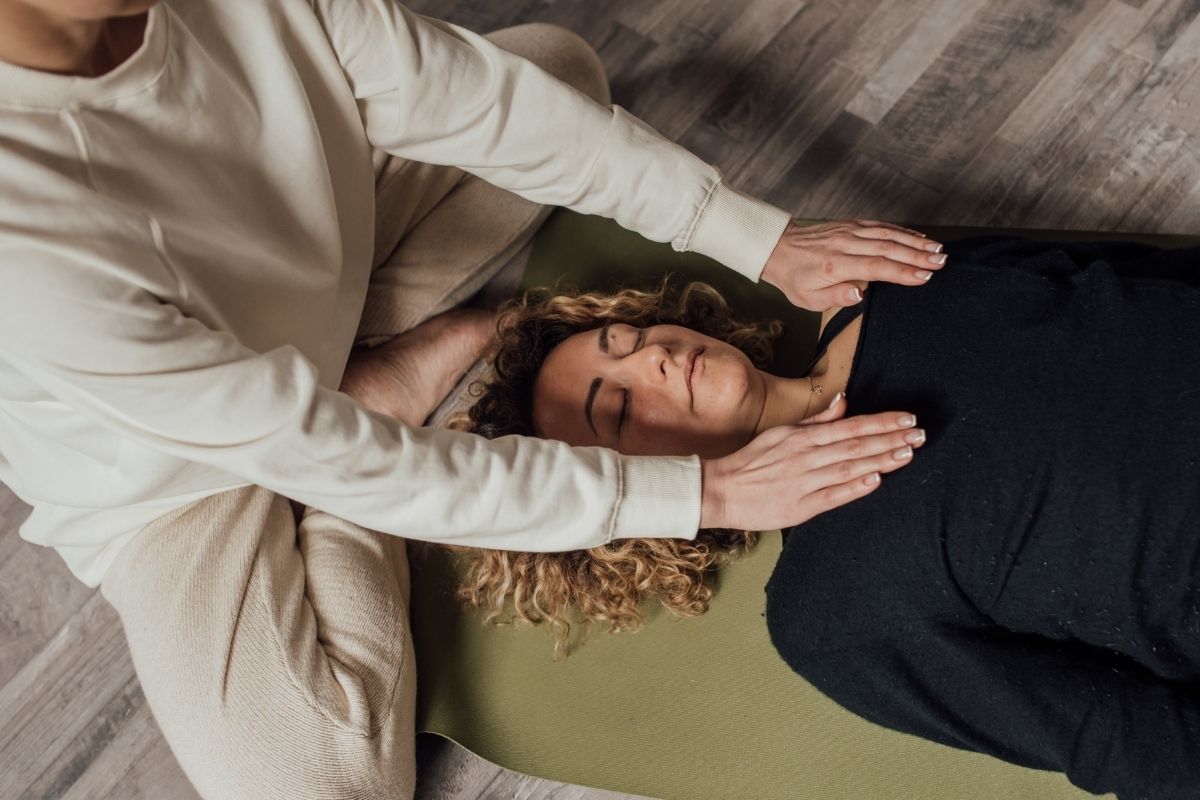 Practitioner performing somatic therapy on a woman lying on a mat with eyes closed hands placed gently over her chest